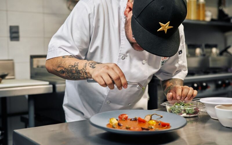 Getatoeëerde chef werkt een kleurrijk gerecht af in de keuken